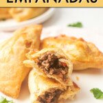 THREE EMPANADAS ON A PLATE, WITH ONE CUT IN HALF TO SHOW THE MEAT FILLING