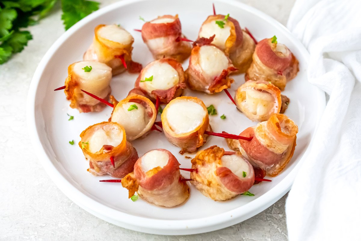 the finished air fryer bacon wrapped scallops on a white plate and garnished with parlsey