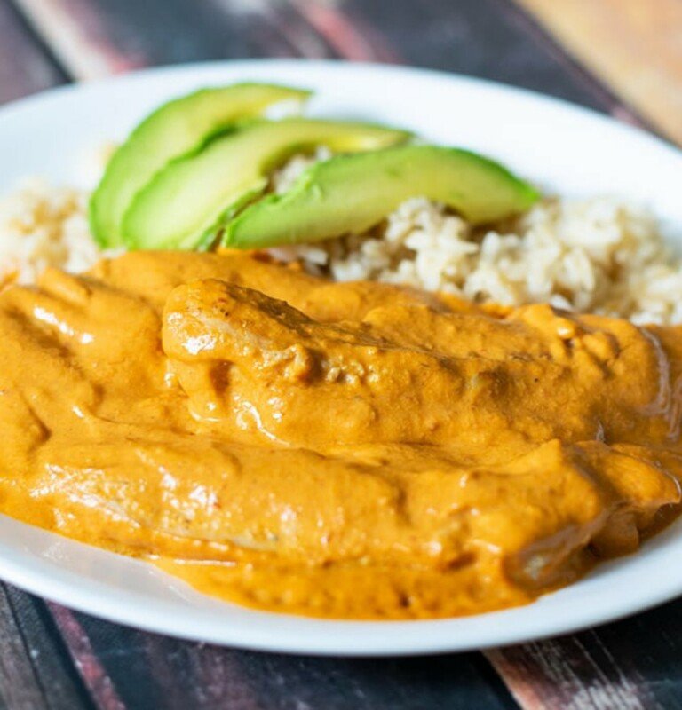 Creamy Chipotle Chicken in a white plate with rice and slices of avocado.