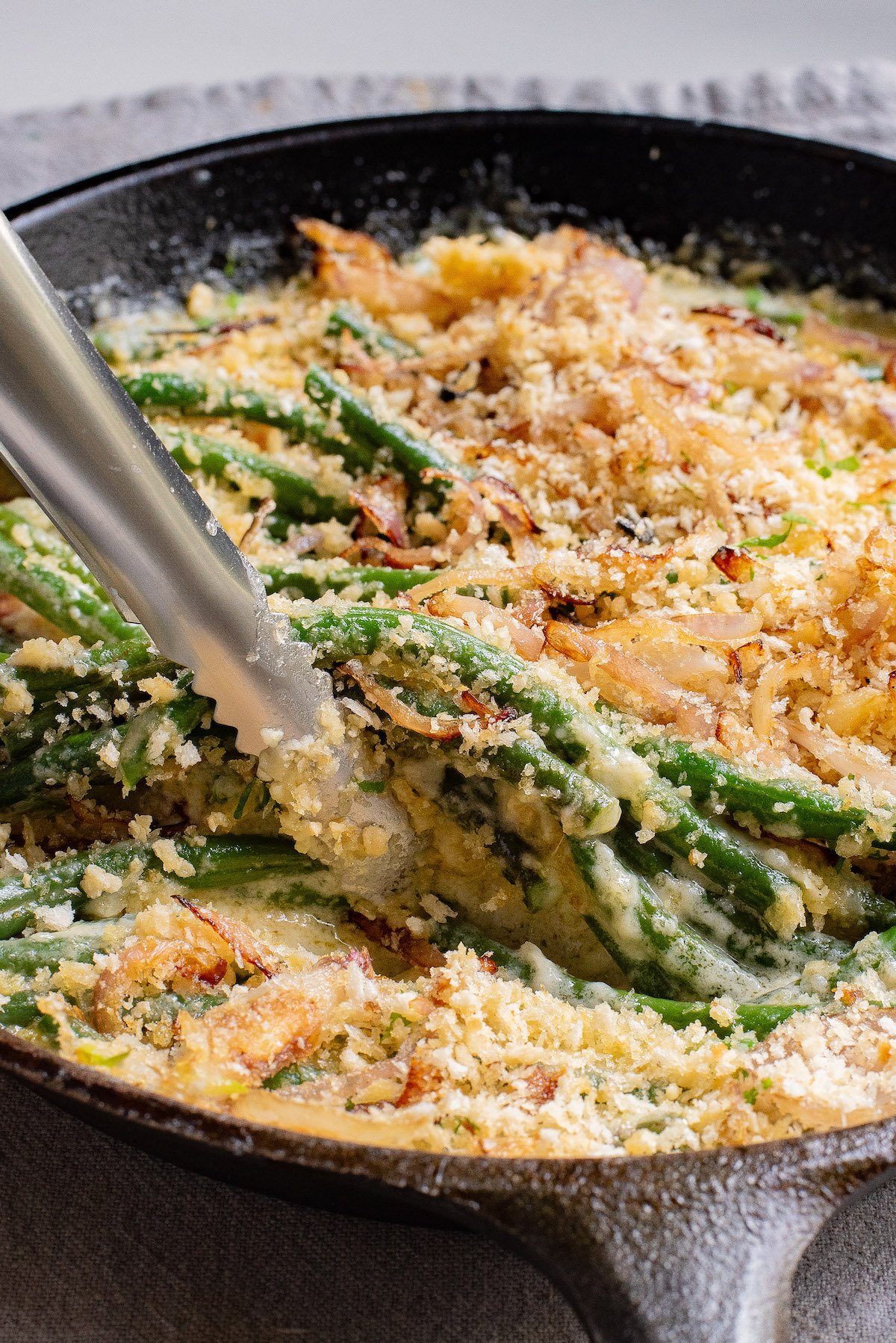 a pair of tongs removing some of the green bean casserole recipe from the skillet