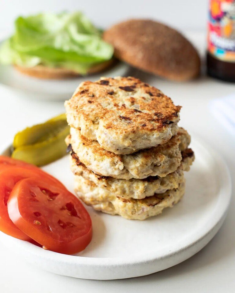 four healthy chicken burger patties stacked on a white plate