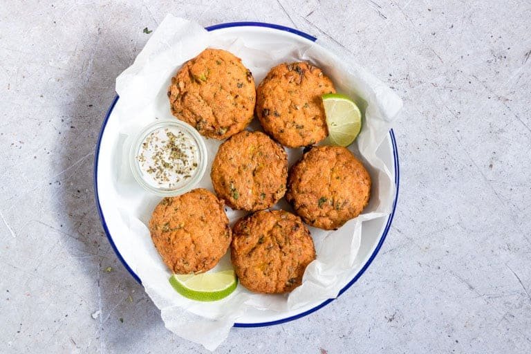 close up of bowl filled with cooked air fryer salmon patties served with lime wedges and a cup of dipping sauce