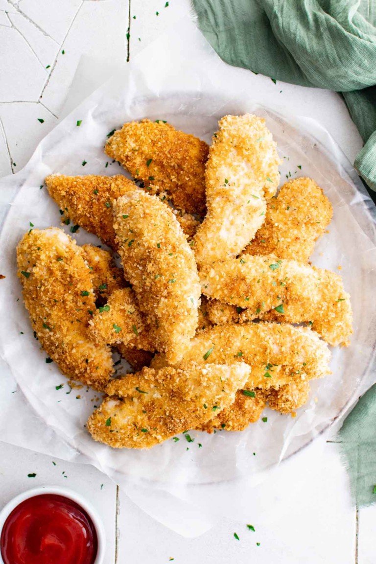 the finished baked chicken tenders on a white plate and served with a side of ketchup a