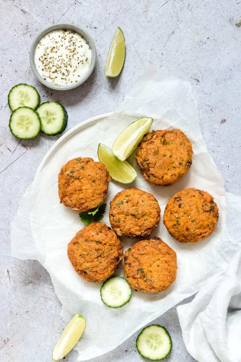 Baked salmon patties served on a white plate with lime wedges, sliced cucumber and homemade dipping sauce