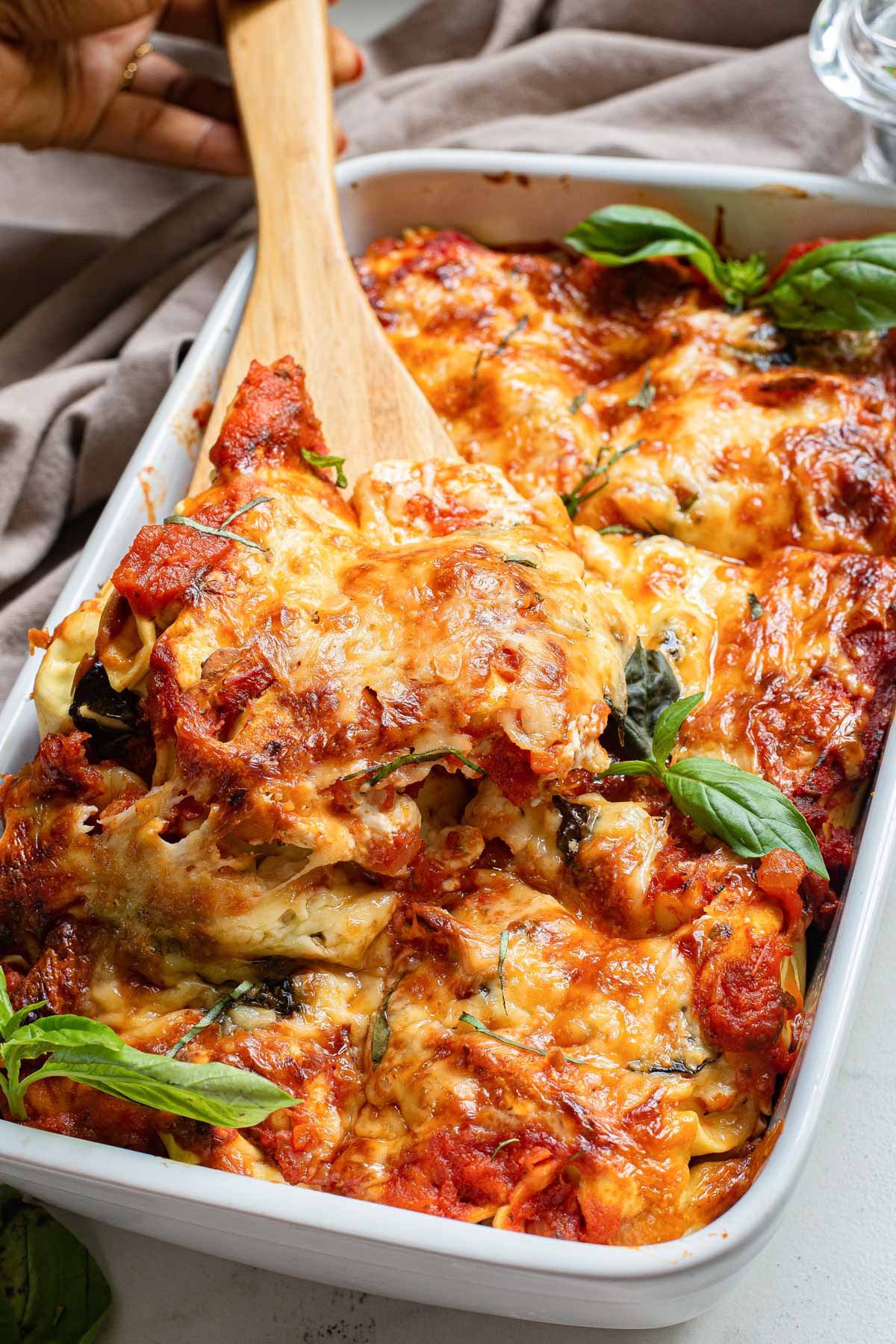 a serving spoon scooping out a portion of the baked tortellini casserole