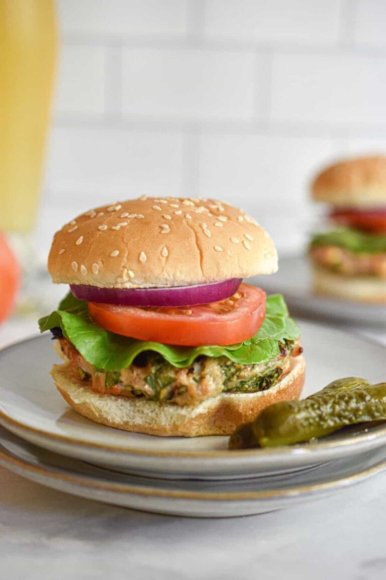 chicken burger with feta and spinach served with a pickle on a white plate