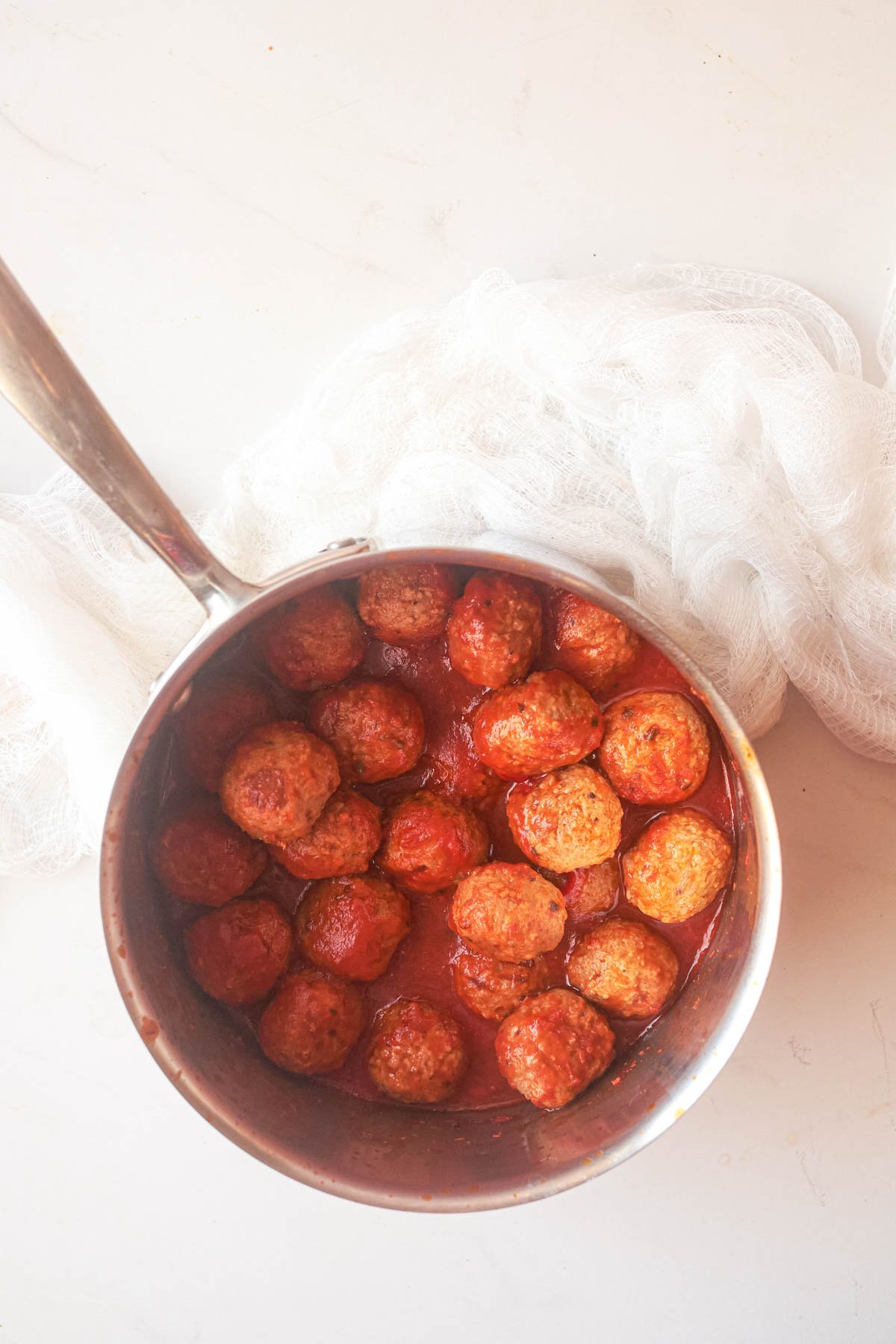 top down view of frozen meatballs in a pan with sauce as part of the how to cook meatballs on stovetop recipe