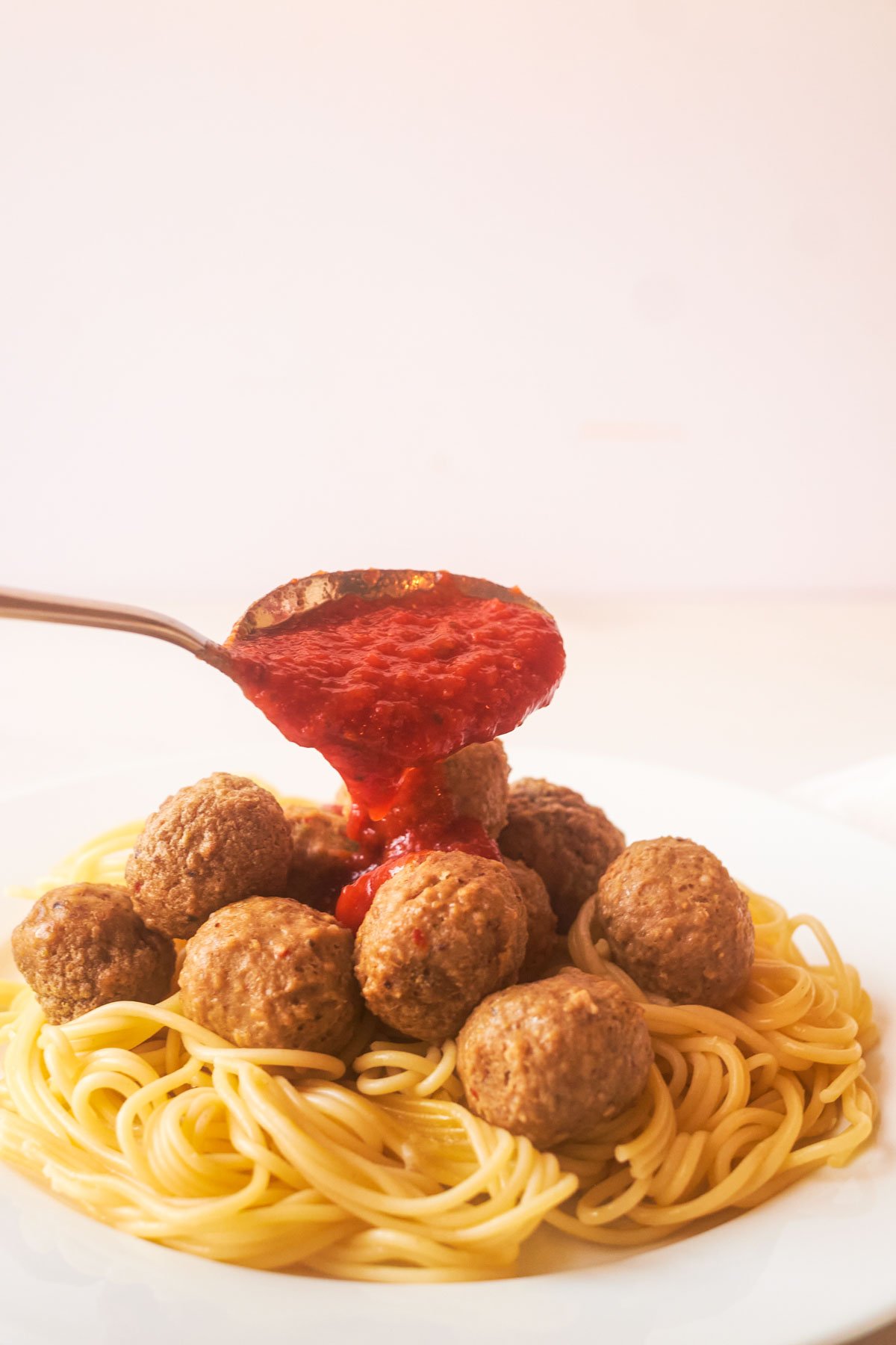 a spoon pouring sauce over cooked frozen meatballs and pasta