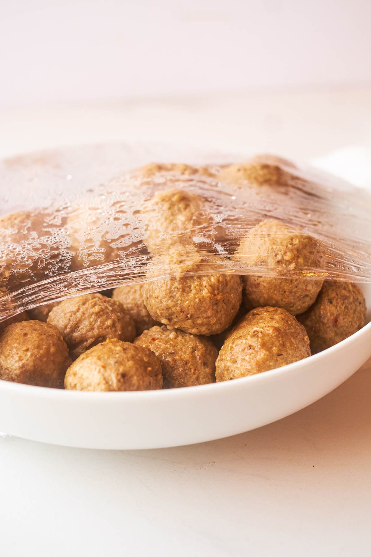 frozen meatballs in a dish covered with plastic wrap to show how to cook frozen meatballs in microwave