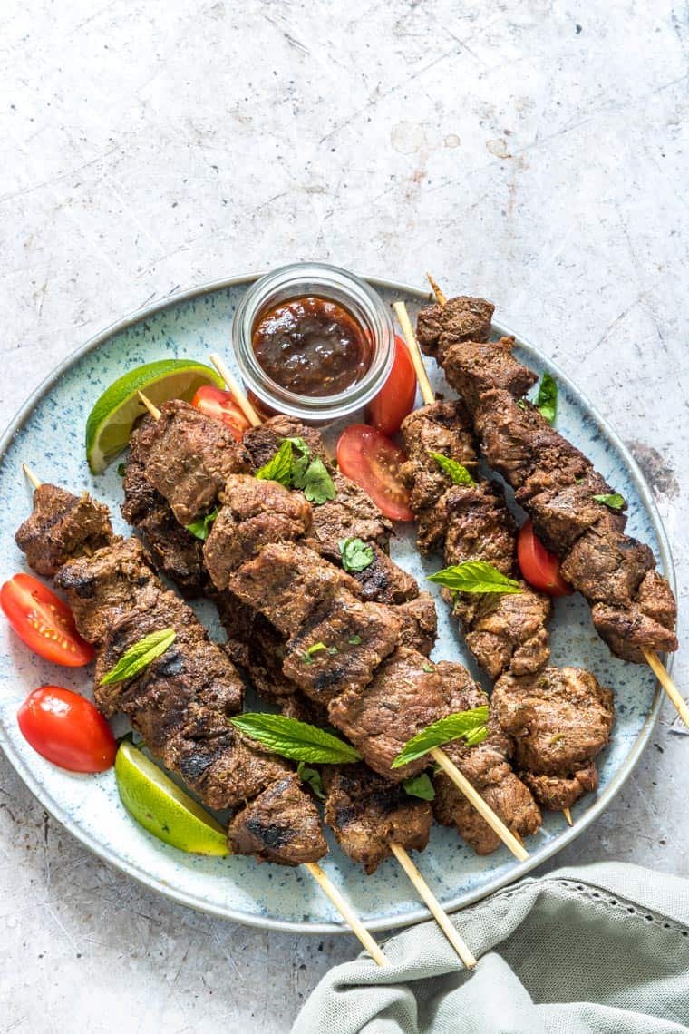 lamb kabobs served with tomatoes and a cup of dipping sauce