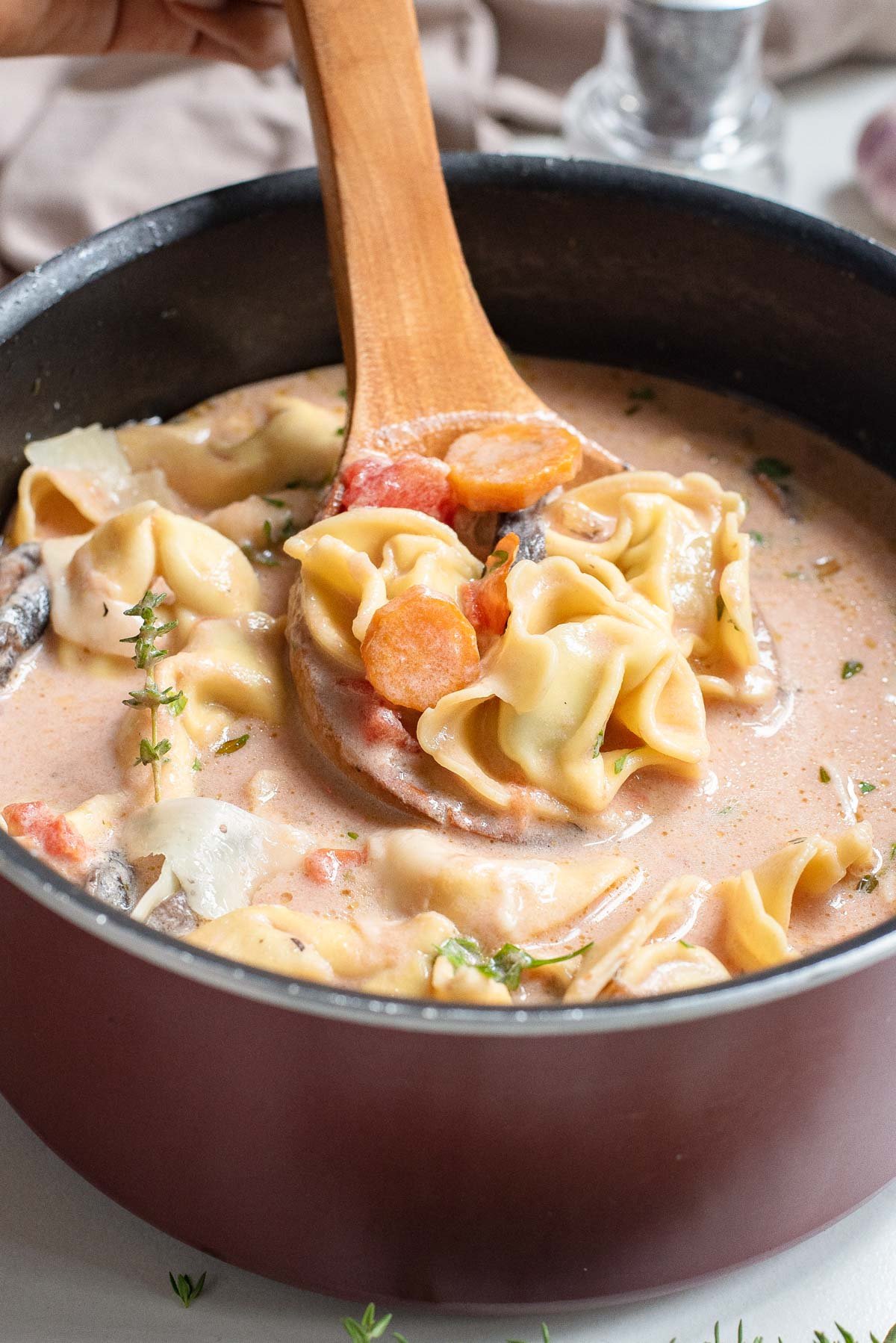 a wooden spoon removing some of the tomato tortellini soup from the cooking pot